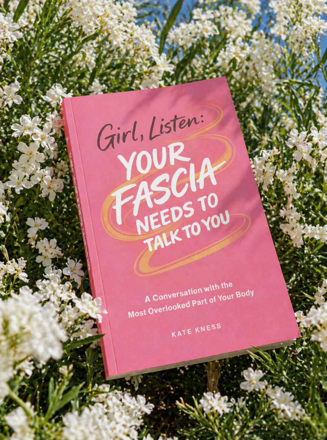 Fascia book Girl, Listen: Your Fascia Needs to Talk to You pink cover styled in flowers Book cover of Girl, Listen: Your Fascia Needs to Talk to You by Kate Kness, a fascia and body awareness book, styled in white flowers outdoors